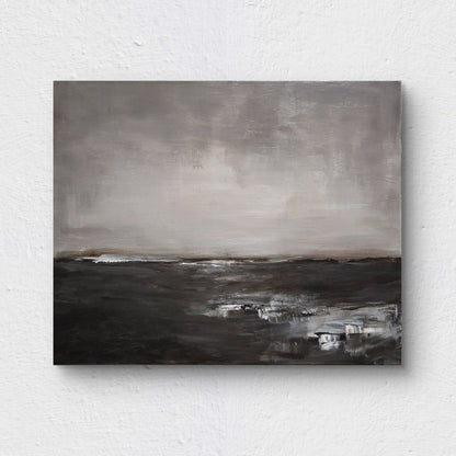An abstract, minimalist landscape painting, rendered in muted shades of gray, white, and deep brown, suggesting a wide, bleak expanse of land or water meeting a vast, overcast sky. Painting is on a white wall.